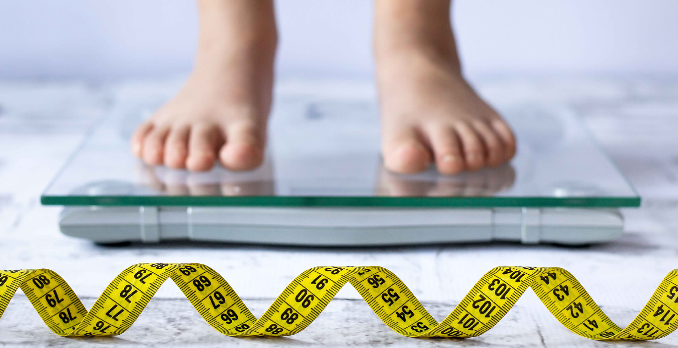 Child on scale with uncoiled tape measure beside it