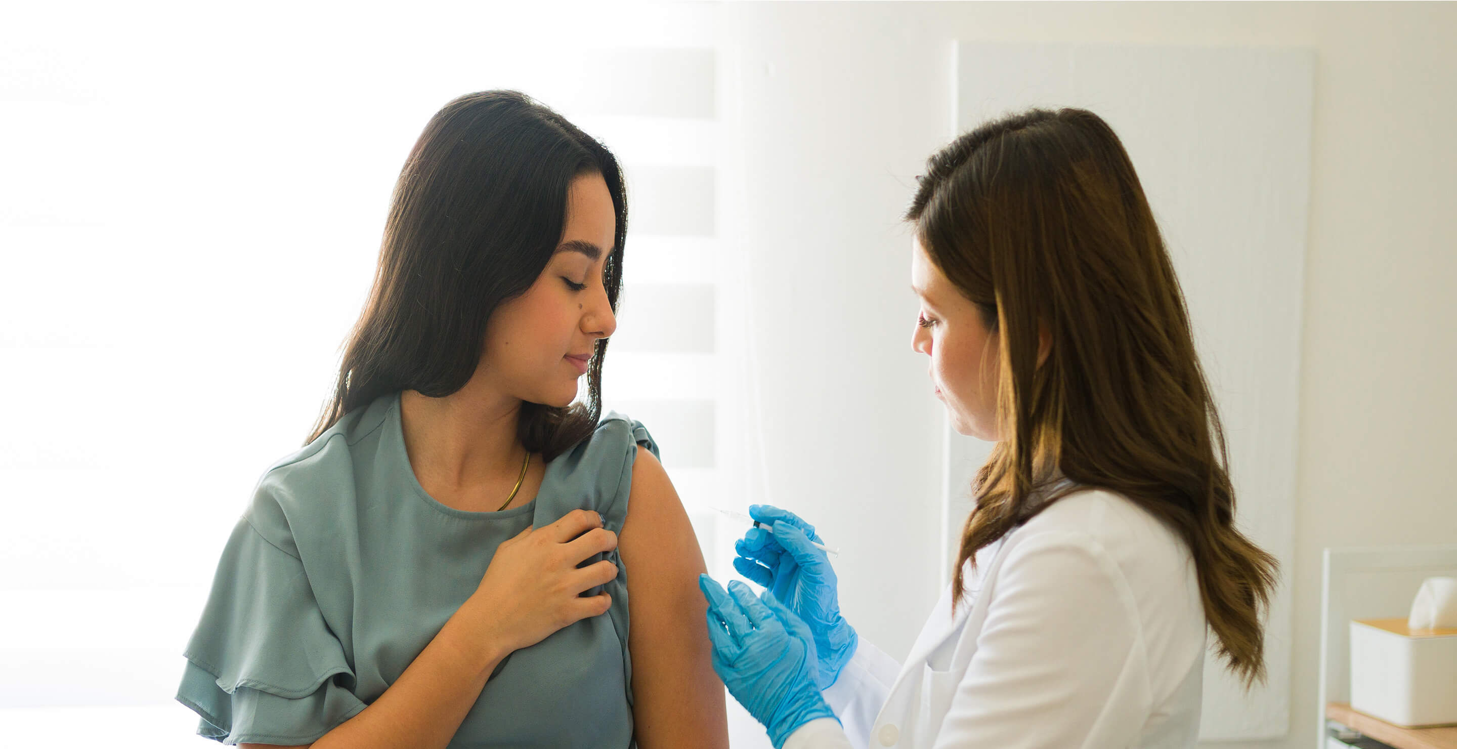 A female patient in hospital gown is receiving an injection from a female doctor